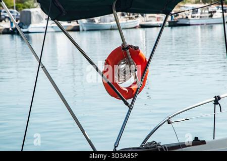 Orangefarbener Rettungsring, Seile und Kotflügel hängen an einem Bootsgeländer im Hafen Stockfoto