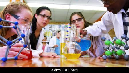 Gießen der blauen Lösung aus dem Becher in den Kolben im Chemielabor mit Labormänteln und Schutzbrillen Stockfoto