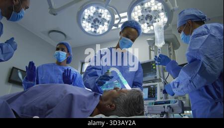 Das mit der Anästhesemaske behandelte Operationsteam überwacht Vitalparameter und IV-Anpassung im OP Stockfoto