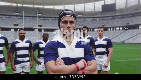 Das posierende Rugby-Team trägt blau-weiß gestreifte Trikots und gepolsterte Kopfbedeckungen auf dem Rasen mit Torpfosten Stockfoto