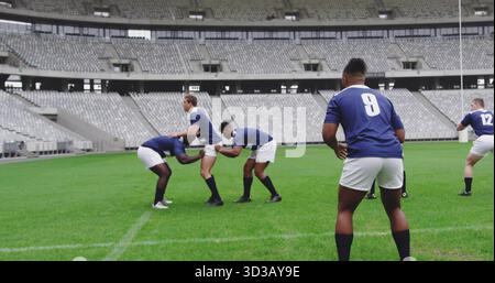 Sie bilden sieben männliche Athleten, die im leeren Stadion Scrum üben, mit blauen Trikots und weißen Shorts Stockfoto