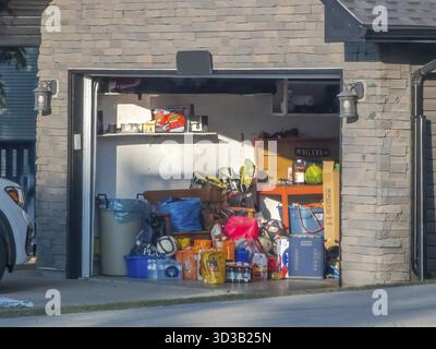 Calgary, Alberta, Kanada. Juni 2025. Eine sonnendurchflutete Garage steht offen und offenbart ein Ungewirr an Haushaltsgegenständen, Aufbewahrungsbehältern und deutet auf einen Bedarf an organischem Material hin Stockfoto