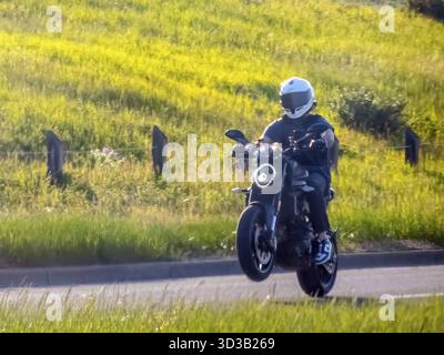 Calgary, Alberta, Kanada. Juni 2025. Ein Motorradfahrer auf einem schlanken dunklen Motorrad führt einen Wheelie auf einer Asphaltstraße durch und bietet aufregende Leistung und Stockfoto