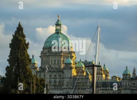 Victoria, British Columbia, Kanada. Februar 2025. Die Parlamentsgebäude von British Columbia in Victoria, in warmes Sonnenlicht getaucht, mit einem Segelboot-Mast Stockfoto