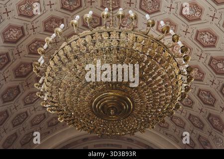 Essen, eleganter goldener Kronleuchter mit detaillierten Mustern, die unter einer wunderschön verzierten, dekorierten Decke hängen und komplizierte Kunst und Luxus zeigen Stockfoto