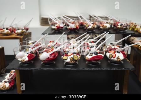 Essen, klare Tassen gefüllt mit Joghurt, Müsli und frischen Beeren, ordentlich auf einem Catering-Buffet-Tisch Stockfoto