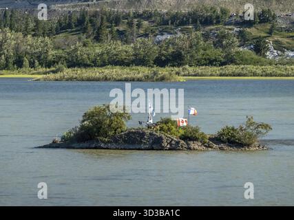 Eine kleine, mit Bäumen bewachsene Insel in einem ruhigen See, die mit Flaggen für verschiedene Länder geschmückt ist, deutet auf eine friedliche und internationale Zusammenkunft hin Stockfoto