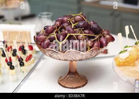 Speisen, ein paar reife rote Trauben in einer dekorativen Glasschale auf einem weißen Tisch, ideal für Obstplatten oder Buffets Stockfoto