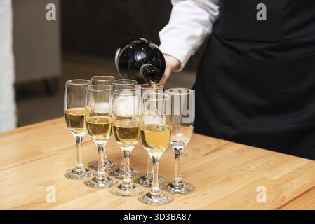 Essen, der Kellner gießt während einer festlichen Veranstaltung oder Party Sekt in eine Reihe Sektflöten auf einem Holztisch Stockfoto