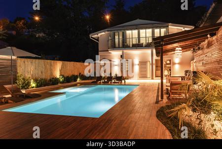 Eleganter Hinterhof mit beleuchtetem Swimmingpool und gemütlichen Sitzgelegenheiten im Freien Stockfoto