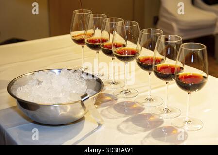 Essen, mehrere Weingläser werden auf einem weißen Tisch mit Rotwein gefüllt, neben einer Metallschale mit Eiswürfeln Stockfoto