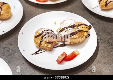 Essen, zwei Cremesuppen mit Puderzucker und Schokoladensauce, serviert mit frischen Erdbeerscheiben auf einem weißen Teller Stockfoto