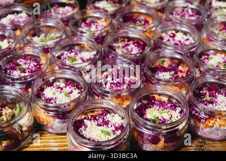 Speisen, bunte Salate mit Rote-Bete- und Karottenschicht, garniert mit zerbröckeltem Käse, serviert in kleinen Glasgläsern für Catering-Veranstaltungen Stockfoto