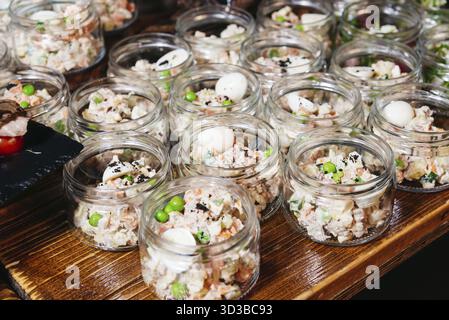 Essen, Mini-Gläser gefüllt mit cremigem Gemüse- und Fleischsalat, garniert mit grünen Erbsen und Wachteleiern, perfekt für Catering-Veranstaltungen Stockfoto