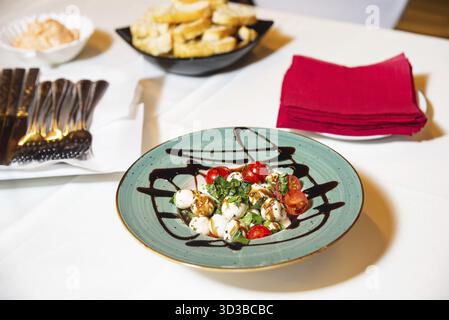 Essen, frischer Caprese-Salat mit Mozzarella-Bällchen, Kirschtomaten, Basilikum und Balsamico-Glasur, serviert auf einem türkisfarbenen Teller Stockfoto