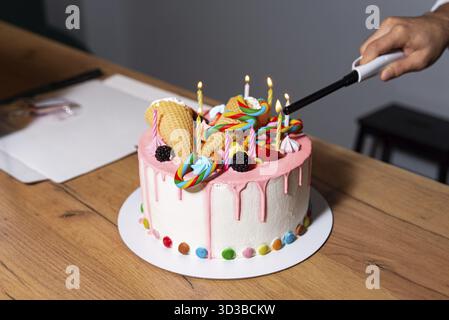 Essen, Handanzünden von Kerzen auf lebendigem Geburtstagskuchen, dekoriert mit Süßigkeiten, Lutscher, Eiskegel und rosa Glasur Stockfoto