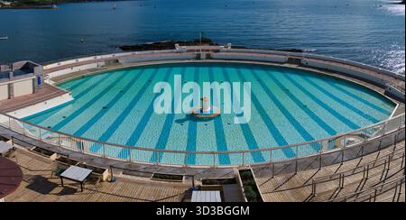 Plymouth, Großbritannien - 25. September 2025: Blick von oben auf den kreisrunden Art déco Tinner Lido in Plymouth, Großbritannien, mit gestreiftem türkisfarbenem Wasser und Plymouth Sound Beyond, aufgenommen an einem sonnigen Nachmittag. Stockfoto
