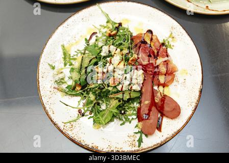 Essen, Ein wunderschön überzogener Rucola-Salat mit pochierten Birnen, Schinken, Blauschimmelkäse, kandierten Walnüssen, Balsamico-Glasur, und Dressing, serviert auf einem Rusti Stockfoto