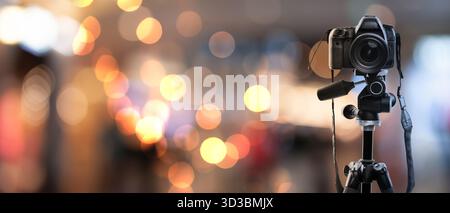 Professionelle Kamera auf Stativ vor verschwommenem Hintergrund mit Bokeh-Lichtern. Bannerdesign Stockfoto