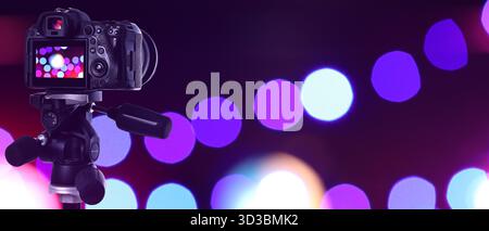 Professionelle Kamera gegen verschwommenes Licht auf dunklem Hintergrund, Bokeh-Effekt. Bannerdesign Stockfoto