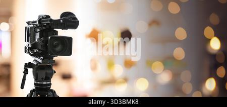 Videokamera auf Standfuß vor verschwommenem Hintergrund mit Bokeh-Lichtern. Bannerdesign Stockfoto