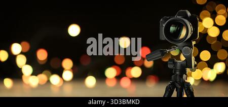Professionelle Kamera auf Stativ gegen unscharfes Licht, Bokeh-Effekt. Bannerdesign Stockfoto