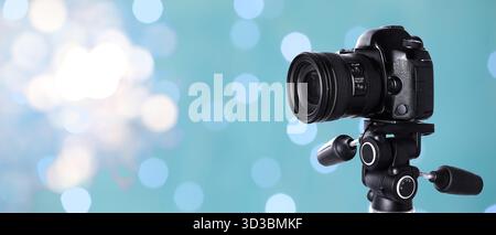 Professionelle Kamera gegen verschwommenes Licht auf hellblauem Hintergrund, Bokeh-Effekt. Bannerdesign Stockfoto