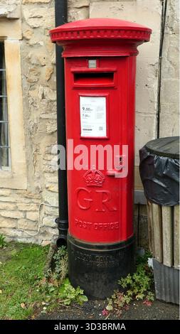 Castle Combe, Vereinigtes Königreich - 17. September 2025 vor einer alten Mauer steht ein original roter Postkasten der Royal Mail Post oder ein Säulenkasten Stockfoto