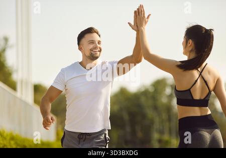 Draußen laufen, fröhliches sportliches Paar, fitter Mann und Frau fröhlich High Fiving, hell lächelnd Stockfoto