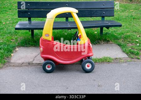 Plastikspielzeugauto parkt draußen auf Asphalt neben einer grünen Parkbank in Haringey North London England N15 KATHY DEWITT Stockfoto
