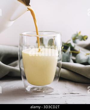 Essen, einen Kaffee mit Milch aus der Teekanne in eine Glasschale gießen Stockfoto