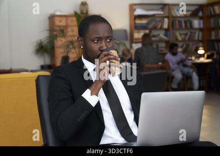 afroamerikanischer Geschäftsmann mit Kaffee, der im Hotel am Laptop arbeitet Stockfoto