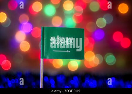Saudische Flagge auf einem hellen, abstrakten Hintergrund mit verschwommenen Regenbogenbokeh-Lichtern. Symbolisiert den Nationalfeiertag, Vision 2030 und das Königreich. Stockfoto
