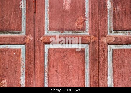 Antike rote Holzstruktur mit geometrischen Paneelen und abblätterndem Farbeffekt. Rustikaler Hintergrund für Vintage- und Innenarchitektur. Stockfoto