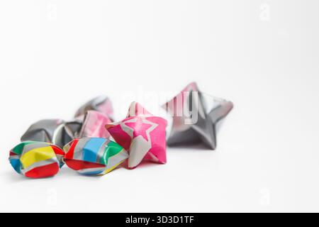 Kleine Gruppe handgemachter Origami-Glückssterne in hellen Farben auf weiß. Erfasst delikates Papierhandwerk und das Konzept von Glück/Freundschaft. Stockfoto