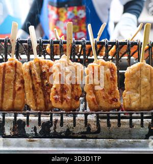Moo Ping (thailändische gegrillte Schweinespieße) kochen auf einem Holzkohlegrill. Ikonisches asiatisches Street Food, ideal für Reisen, thailändische Küche und Grillthemen. Stockfoto