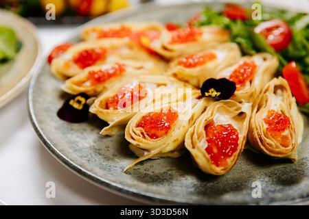 Festliche Krepprollen mit rotem Kaviar, Grün und Kirschtomaten auf elegantem Tisch Stockfoto