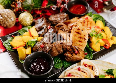 Gegrilltes Fleisch und Kartoffeln mit Sauce auf festlichem Festtisch Stockfoto