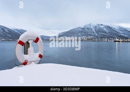 Rettungsring abgedeckt im Schnee am Ufer des berühmten tromso Brücke über Tromsoysundet Strait, Nördliches Norwegen Stockfoto