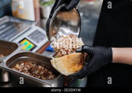 Der Koch bereitet ein Shawarma-Sandwich mit gegrilltem Fleisch und frischem Gemüse in Pitabrot zu Stockfoto