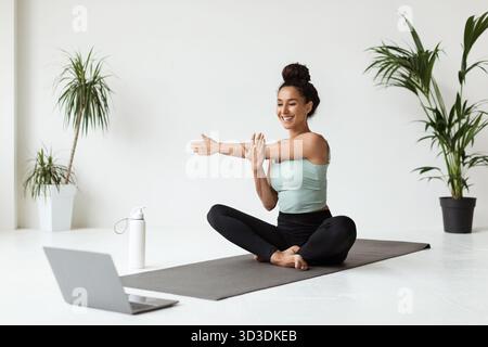 Schöne junge Frau dehnt sich zu Hause, während sie online in Activewear trainiert Stockfoto