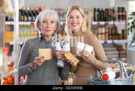 Zwei Käuferinnen mit verschiedenen Milchprodukten in den Händen treffen weiterhin die Wahl in der Lebensmittelabteilung des Supermarktes Stockfoto