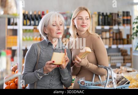 Die Erwachsene Tochter hilft älteren Müttern, im Supermarkt leckeren Käse zu wählen Stockfoto