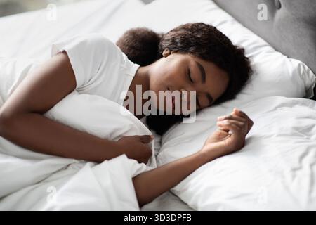 Junge Schwarze Frau, die friedlich allein in einem komfortablen Bett zu Hause schläft Stockfoto