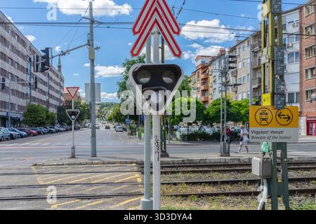 Warnschild an einem Bahnübergang der Budapester H5-Vorortbahn mit Gleisen, Freileitungen und einem Fußgängerübergang. Stockfoto