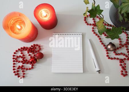 Gefütterter Notizblock, rote Kerzen und Weihnachtsdekoration auf einem weißen Tisch, Mock-up für eine To-do-Liste, Einkaufsliste oder Wunschliste für die Feiertage, Kopien s Stockfoto