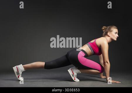 Junge Frau, die ein Fitness-Outfit trägt, dehnt sich aus und blickt weg auf schwarzem Studiohintergrund Stockfoto