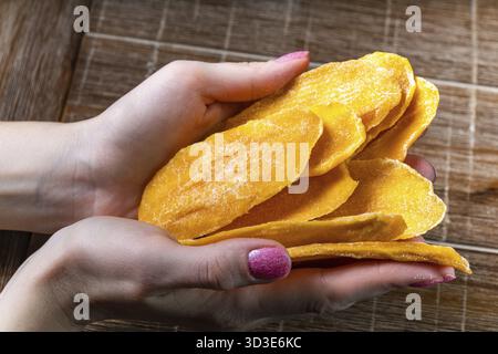 Junge Frau, die getrocknete Mango auf Tischhintergrund in den Händen hält Stockfoto