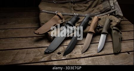 Taktische Messer und Hüllen mit fester Klinge auf einem rustikalen Holztisch und Leinentasche. Stockfoto