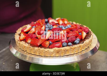 Essen, frische Obsttörtchen mit Schokoladenfüllung und Nusskruste mit Erdbeeren, Himbeeren und Heidelbeeren auf einem Servierstand Stockfoto